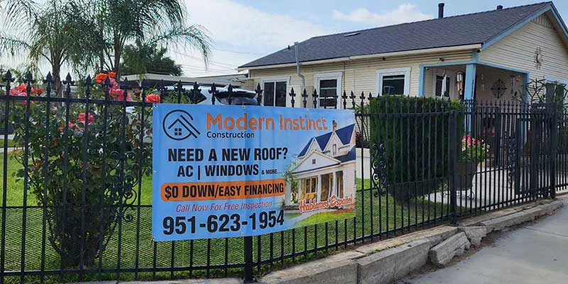Modern Instinct Construction company info banner hanging on a fence surrounding a small residential home